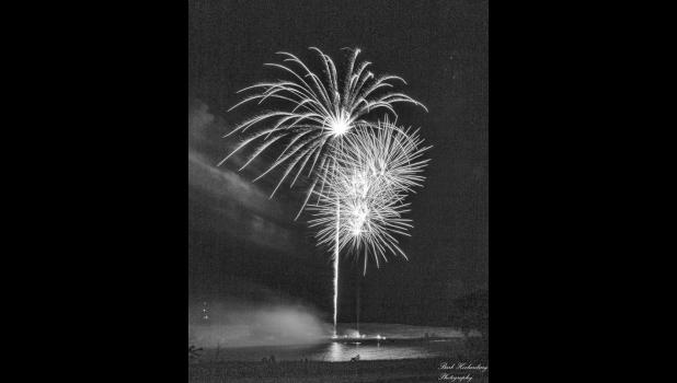 This photo was captured by Barb Hockenbary, displaying the fireworks with the lights of the fire department down below reflected on the North Dam. Photo by Barb Hockenbary Photography